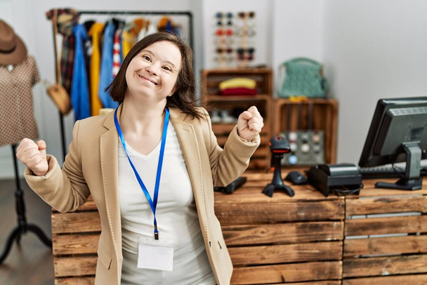 Mujer joven síndrome de Down que trabaja como gerente en boutique minorista muy feliz y emocionado haciendo gesto ganador con los brazos levantados, sonriendo y gritando por el éxito. concepto de celebración.  - Foto, imagen