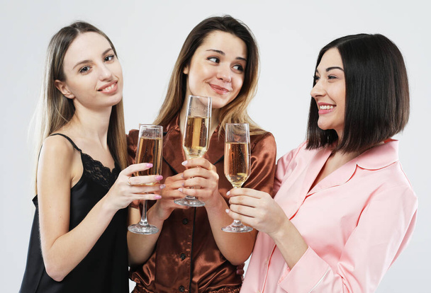 three young beautiful women dressed in pajamas drink champagne and have fun, pajama party and friendship concept. - Photo, image