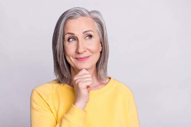 Photo of sweet thoughtful age woman dressed yellow outfit smiling arm chin looking empty space isolated grey color background - Foto, afbeelding
