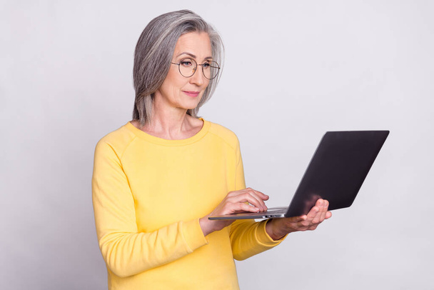 Photo of serious concentrated mature businesswoman working online in computer isolated on grey color background - Foto, afbeelding