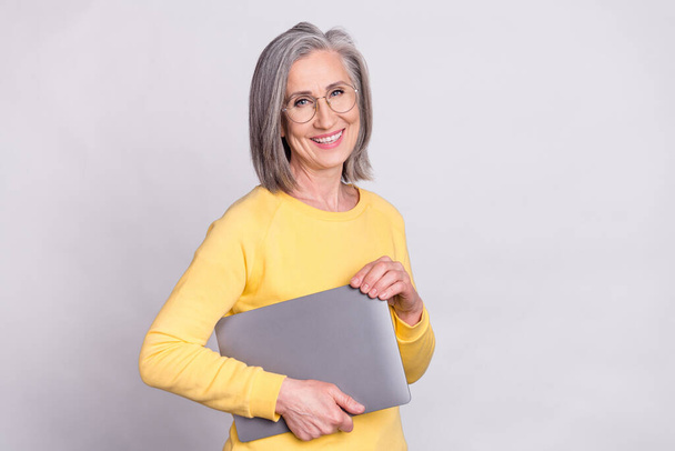 Photo of happy good mood cheerful mature woman in glasses hold laptop wear yellow sweater isolated on grey color background - Фото, зображення