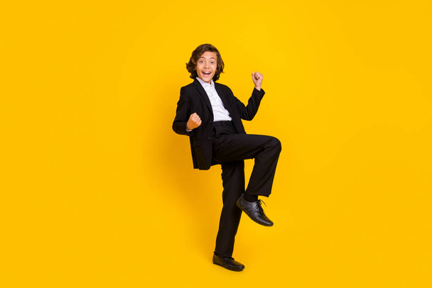 Photo of astonished crazy boy raise fists scream yeah wear black uniform isolated yellow color background - Foto, imagen
