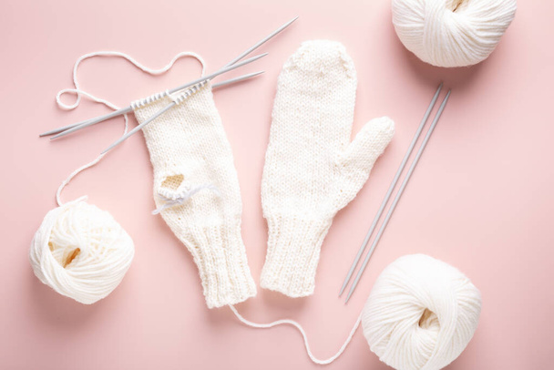 White wool knitting needles and knitted hat on pastel pink background. Female hobby knitting. Top view - Foto, Imagem