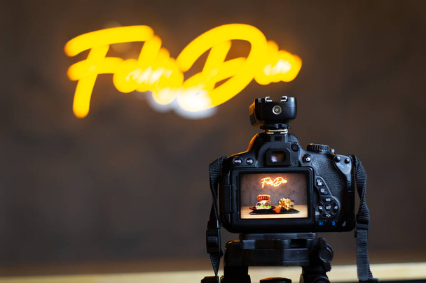 επαγγελματική κάμερα μπροστά από μια κίτρινη πινακίδα νέον με ένα φρέσκο burger μπροστά - Φωτογραφία, εικόνα