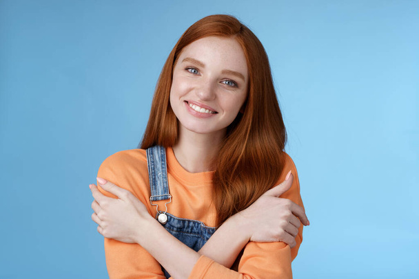 Tender silly redhead girl standing blue background smiling joyfully hugging arms crossed body feel chilly grinning delighted talking boyfriend romantic date asking lend jacket cold summer evening - Foto, afbeelding