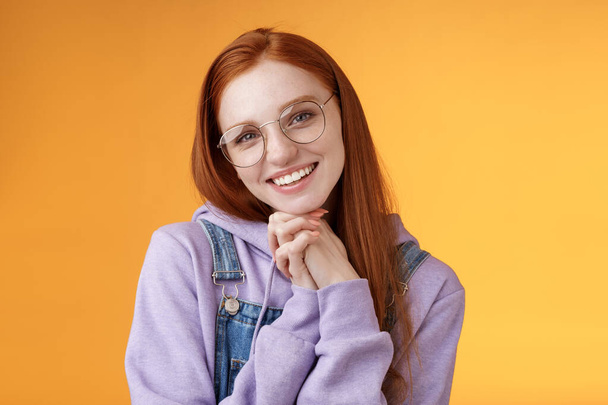 Tender romantic lovely redhead girlfriend leaning palms tilting head cute flirty giggling smiling camera white teeth wearing glasses hoodie overalls near orange background, sensually laughing - Foto, imagen