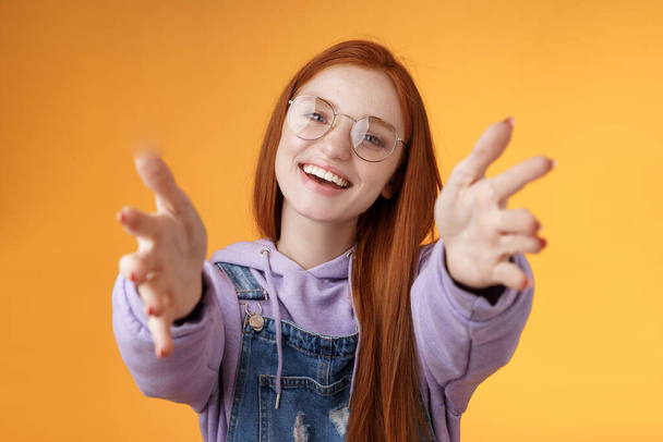 Come here let hold. Attractive silly friendly happy smiling redhead woman stretch arms camera grab product wanna tight friendship hugs grinning embracing cuddling besties, orange background - Photo, Image