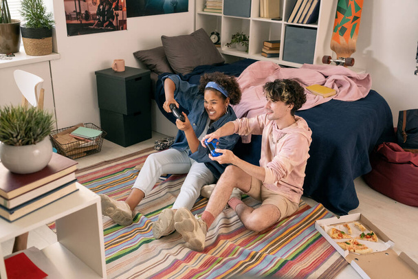 Adolescentes contemporáneos sentados en el suelo y jugando videojuegos - Foto, Imagen