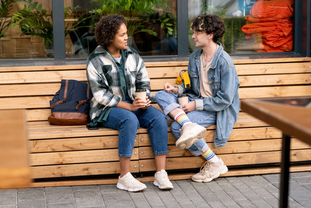 Cute teenage girl and her boyfriend having drinks on wooden bench - Fotó, kép