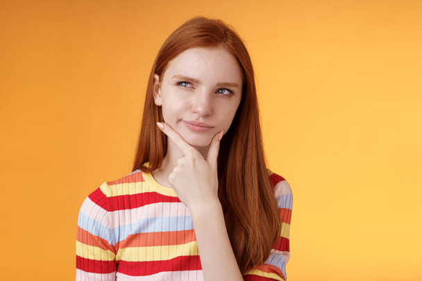 Hmm interesting. Suspicious doubtful attractive european redhead female pondering choice look hesitant thoughtful touch chin smirking tricky look upper left corner thinking, take decision - Photo, Image