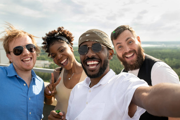 Quatro jovens interculturais sorridentes fazendo selfie enquanto desfrutam de festa - Foto, Imagem