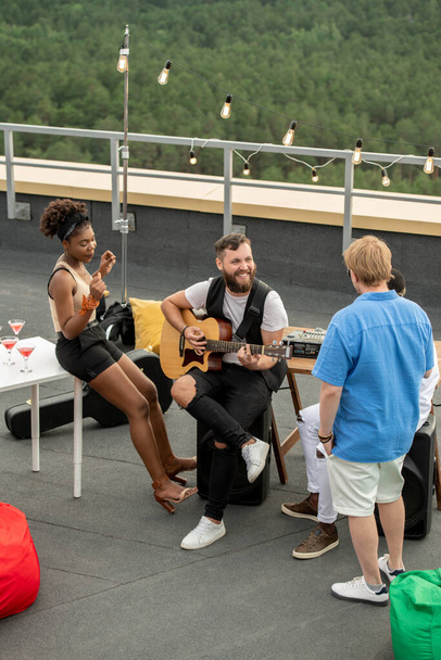 Junge interkulturelle Freunde in Freizeitkleidung plaudern und amüsieren sich auf der Dachterrasse - Foto, Bild