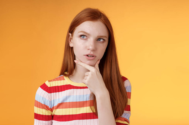 Smart creative serious-looking redhead female coworker thinking deep focus pondering idea making choice touching chin thoughtful look upper left corner questioned puzzled orange background - Foto, Imagen