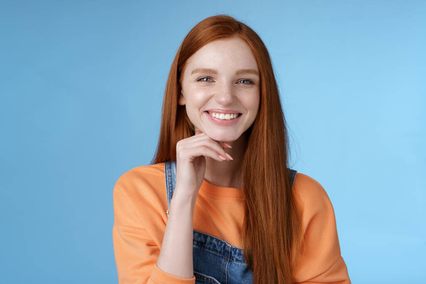 Stylish confident happy smart creative redhead girl look delighted thoughtful like interesting suggestion touch chin smiling approval friendly talking, standing blue background wear overalls - Fotoğraf, Görsel