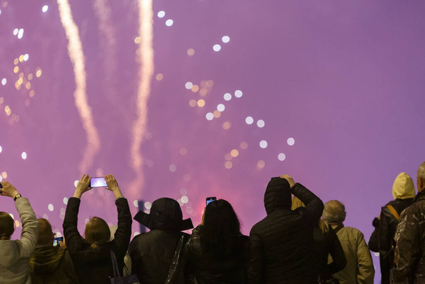 Vista das costas em pessoas em roupas wark disparando fogos de artifício no telefone à noite fria. - Foto, Imagem