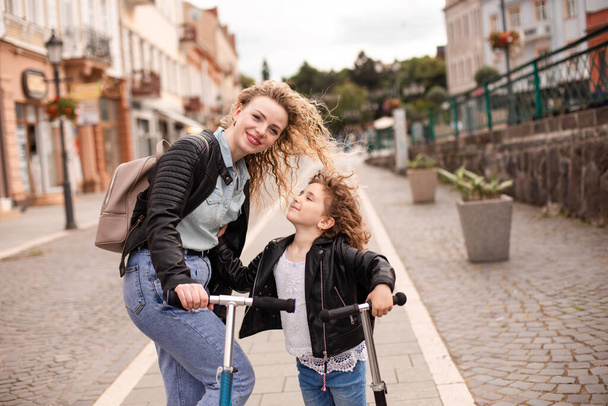 Identical mom and daughter with scooters in the city - Fotó, kép