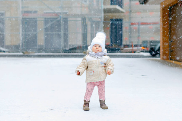 Küçük mutlu kız kışın ilk adımlarını dışarıda, karda atıyor. Yürümeyi öğrenen tatlı çocuk. Soğuk karlı bir günde çocuk eğleniyor. Bebek ilk kar, aktivite. Kış yürüyüşü - Fotoğraf, Görsel