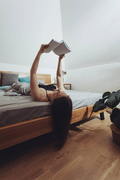 Young girl cant stop reading, lying in bed on her back - Fotografie, Obrázek