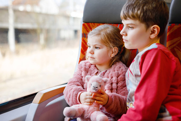 Jolie petite fille tout-petit et petit frère garçon assis dans le train et regardant par la fenêtre. Deux adorables enfants heureux et en bonne santé s'amusent ensemble. Des frères et sœurs souriants partent en vacances en famille par chemin de fer - Photo, image