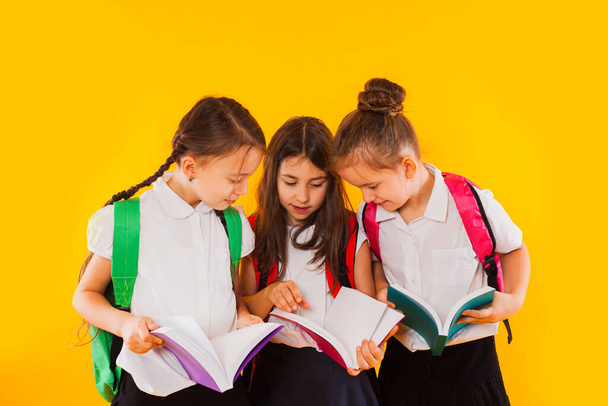 The little schoolgirls are reading the books at the yellow background - 写真・画像