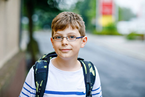 Happy little kid boy with satchel and eyeglasses. Schoolkid wearing glasses on the way to middle or high school. Excited child outdoors on school yard. Back to school. - Foto, imagen