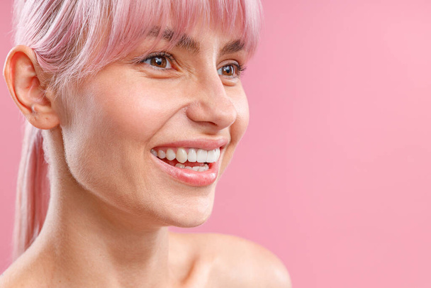 Close up portrait of lovely young woman with pink hair and fresh glowing skin smiling away, posing isolated over pink background - Foto, Imagen