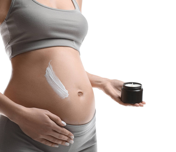 Pregnant woman applying cosmetic product on belly against white background, closeup - Фото, изображение