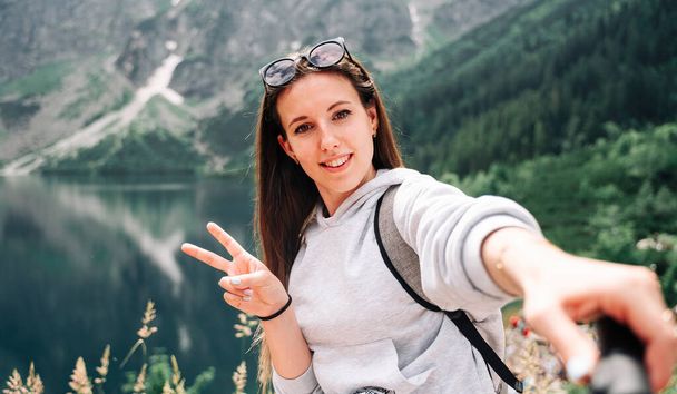 旅行の影響力者。夏の自然を背景にスマートフォンで美しい若い女性ブロガー.山の岩の風景。旅行とフリーランス、現代的なライフスタイルのコンセプト - 写真・画像