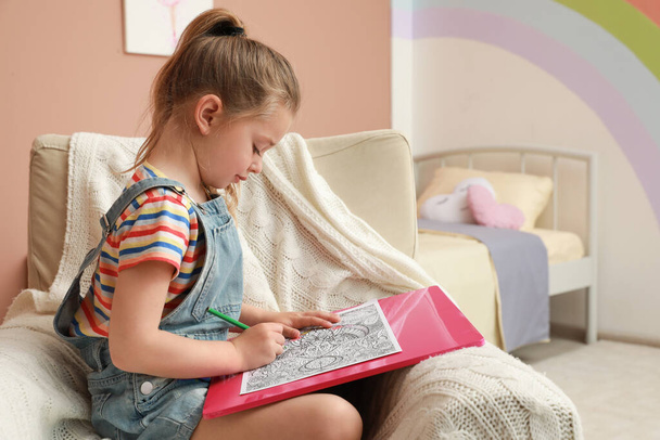 Little girl coloring antistress page in armchair indoors - Fotó, kép