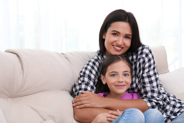 Portrait of happy mother and daughter on sofa at home. Single parenting - Фото, изображение