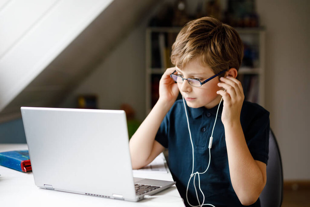 Chłopiec w okularach uczący się w domu na laptopie do szkoły. Urocze dziecko odrabiające lekcje i korzystające z notebooka i nowoczesnych gadżetów. Koncepcja szkolnictwa domowego. - Zdjęcie, obraz