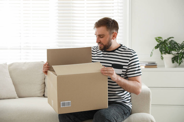 Happy young man opening parcel at home - Photo, image