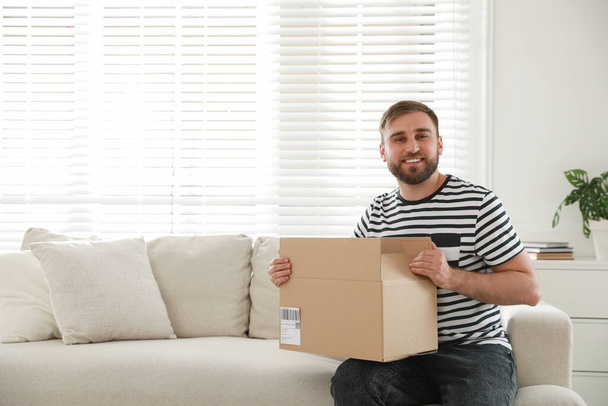 Happy young man with parcel at home - Valokuva, kuva