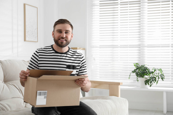 Happy young man with parcel at home - Valokuva, kuva