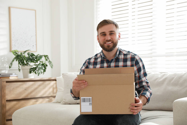 Happy young man with parcel at home - Fotó, kép