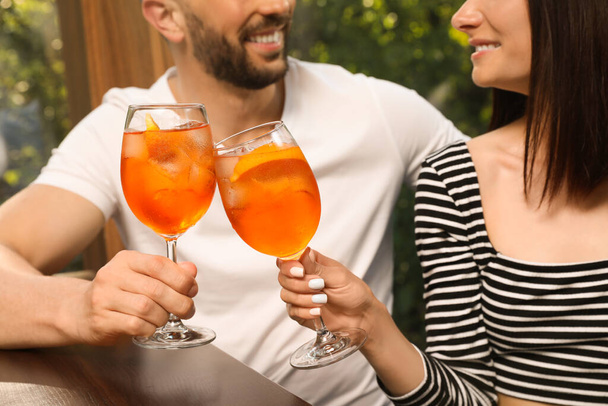 Couple clinking glasses of Aperol spritz cocktails at table, closeup - Foto, imagen