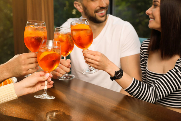 Friends clinking glasses of Aperol spritz cocktails at table, closeup - Fotoğraf, Görsel