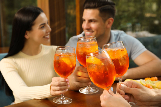 Friends clinking glasses of Aperol spritz cocktails at table, focus on hands - Фото, зображення