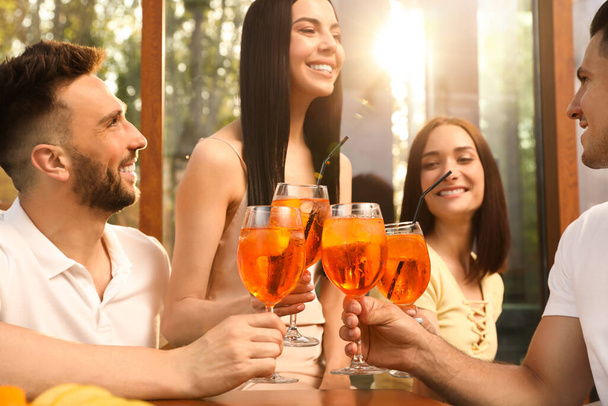 Friends clinking glasses of Aperol spritz cocktails at outdoor cafe - 写真・画像