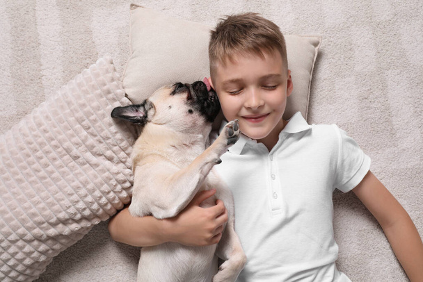 Boy with his cute pug lying on floor at home, top view - Foto, Imagem