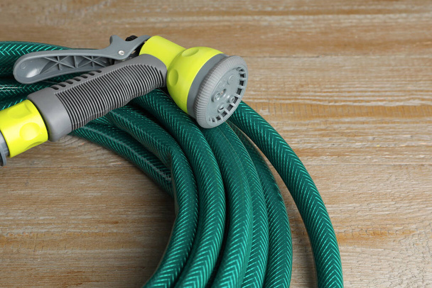 Green rubber watering hose with nozzle on wooden surface, closeup - Foto, immagini