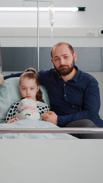 Terapi sırasında hastane koğuşunda kameraya bakan endişeli aile portresi. - Fotoğraf, Görsel