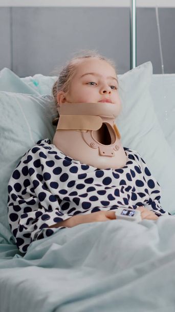 A beteg gyermek beteg beteg portréja, aki az ágyban fekszik, miközben a kamerába néz, miközben nyakörve van. - Fotó, kép