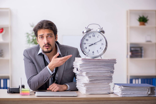 Joven empleado masculino en concepto de gestión del tiempo en el lugar de trabajo - Foto, imagen