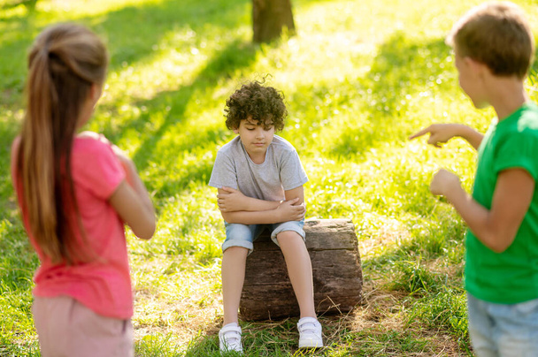 Pensive boy sitting on tree stump and friends - Photo, Image