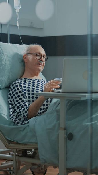 Pacjent na oddziale szpitalnym rozmawiający przez telefon wideo z rodziną - Zdjęcie, obraz