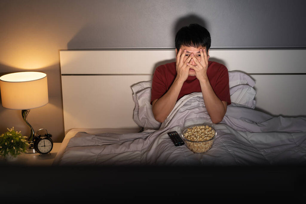 scared young man is watching horror movie TV on a bed at night - Photo, Image