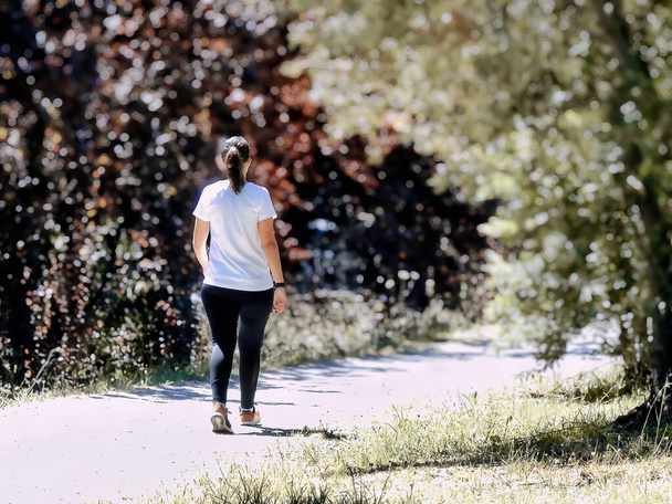 Νεαρή γυναίκα περπατά στο πεζοδρόμιο με θολό φόντο - Φωτογραφία, εικόνα