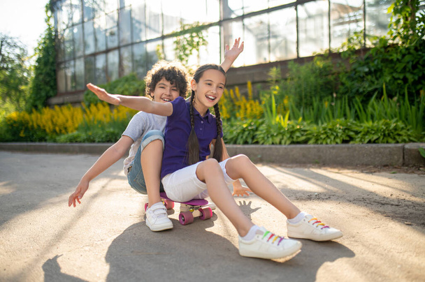 Cheerful boy and girl sitting on skateboard in park - Foto, imagen