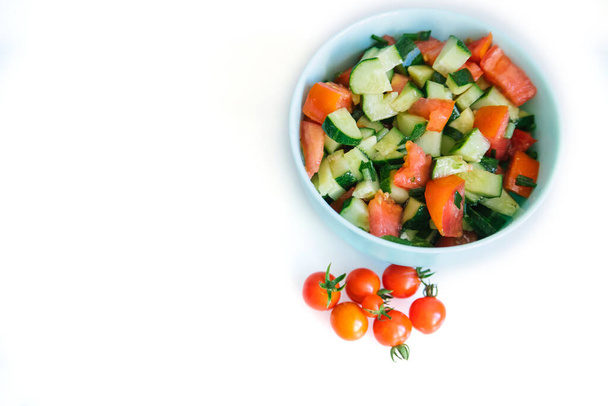 Vegetable salad in a plate on a white background. Chopped onions, tomatoes, cucumbers. Healthy food. Dietary products. Next to it are small cherry tomatoes. - Photo, Image